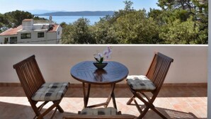 A terrace with two wooden chairs and a table, a bowl of flowers, and a view of the sea and buildings in the background. - Apartments Kovami (Podgora)