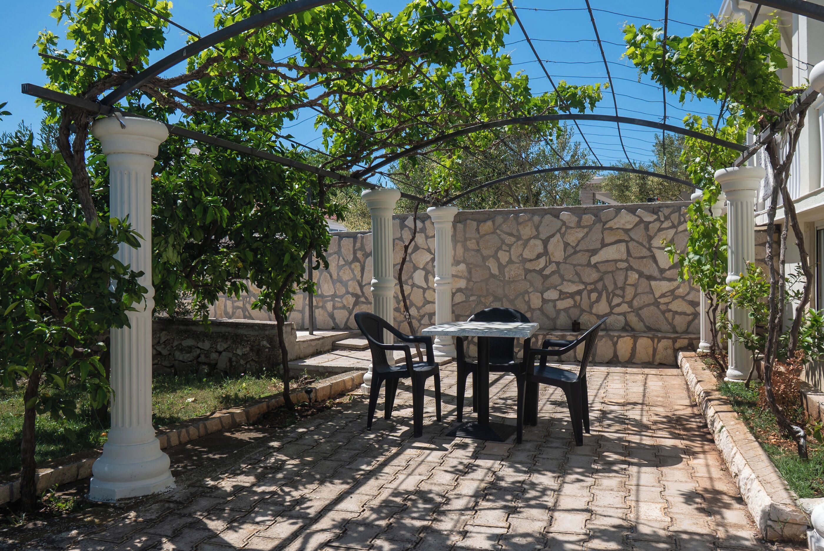 Un patio con pared de piedra, columnas blancas y una mesa con sillas.