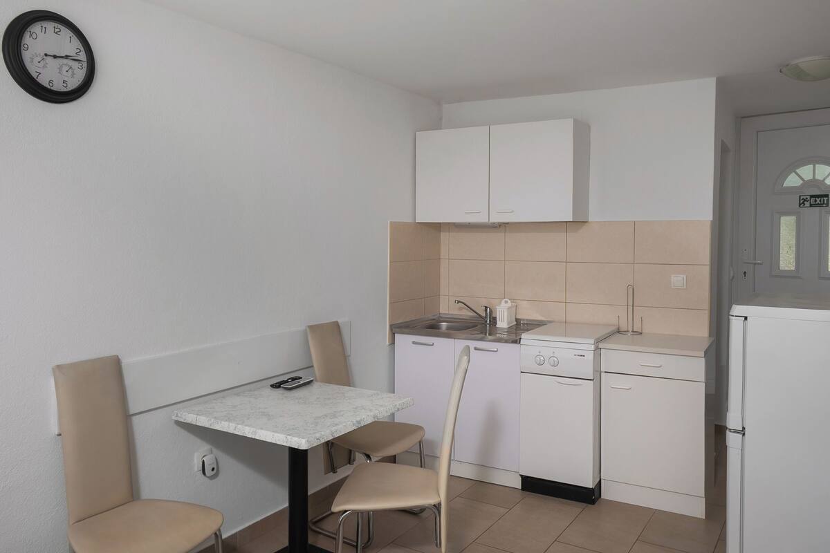 A compact kitchen with a dining area, a clock, and a white cabinet.