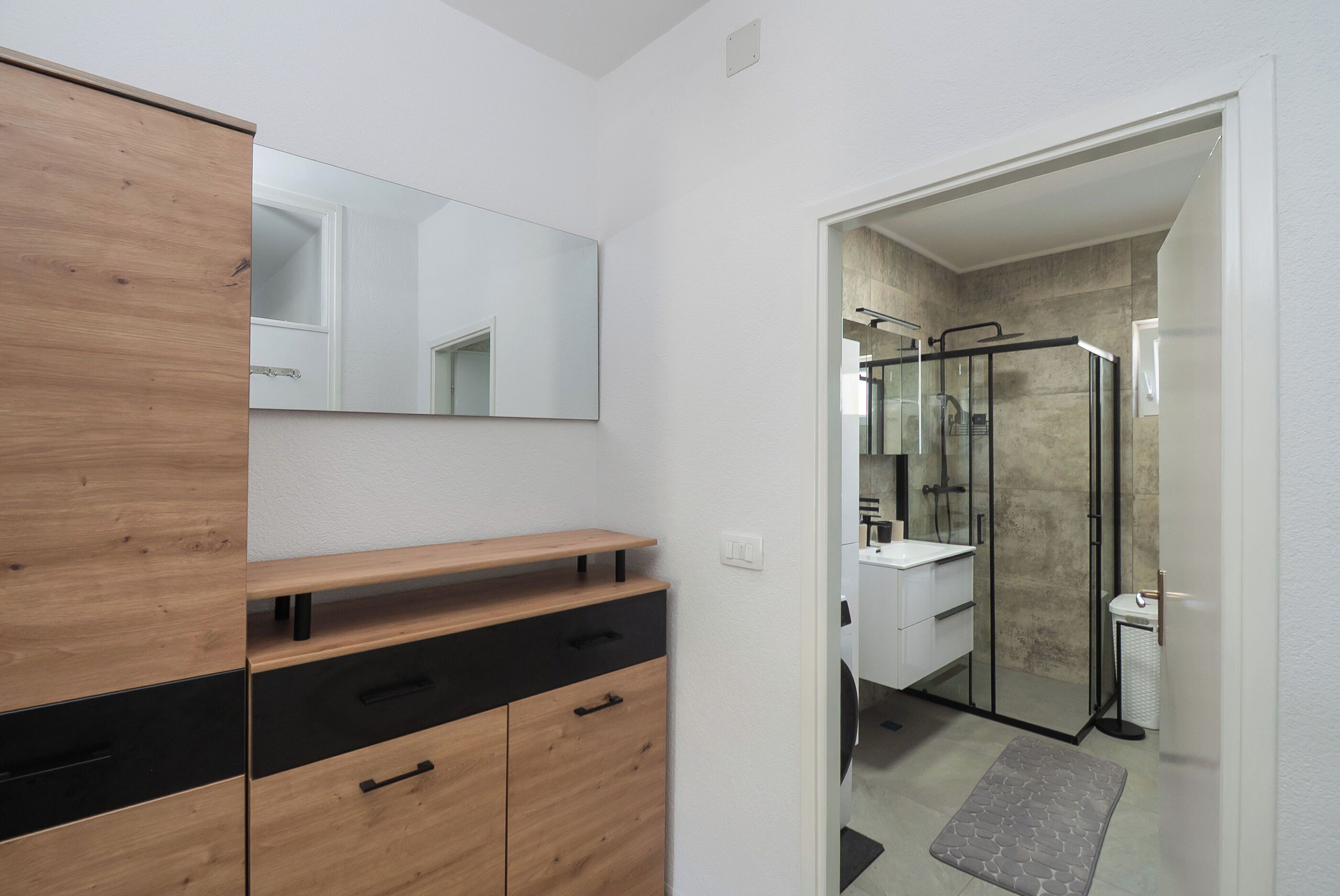A modern bathroom with a wooden vanity, a large mirror, and a glass shower enclosure.