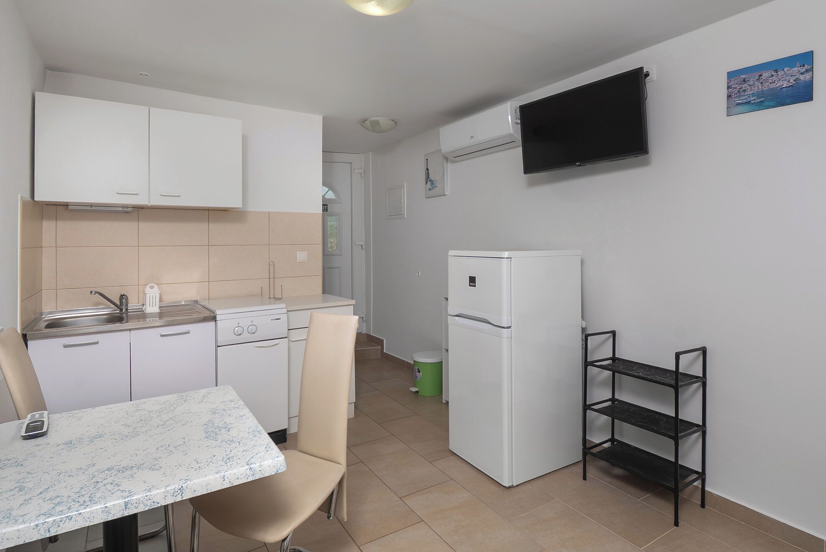 A compact kitchen with white cabinets, a built-in stove, a white refrigerator, and a wall-mounted TV.