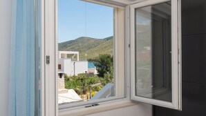 A room with a large window, a view of a hillside, and a glimpse of buildings outside. - Apartments Jadranka (Sibenik)