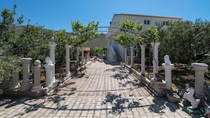 A paved pathway leading to a building with a covered entrance, flanked by white columns and greenery. - Apartments Jadranka (Sibenik)