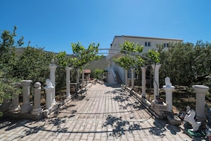 A paved pathway leading to a building with a covered entrance, flanked by white columns and greenery. - Apartments Jadranka (Sibenik)