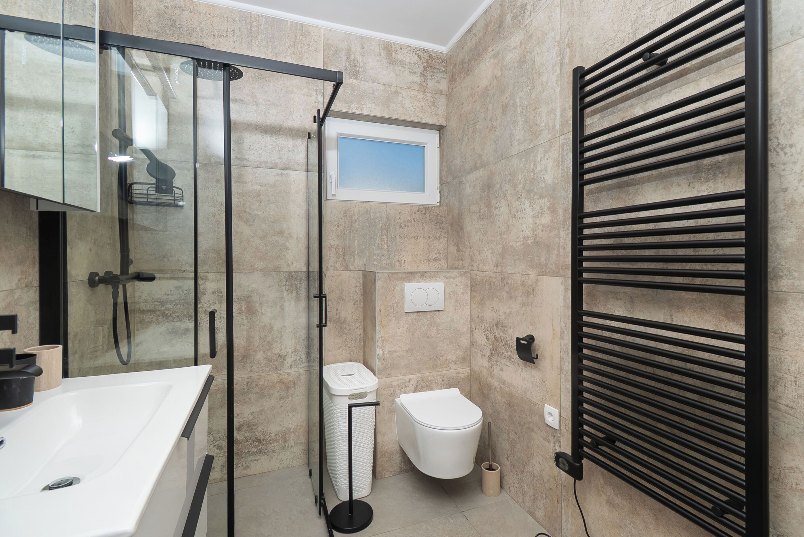 Een badkamer met een douchecabine van glas, een wit toilet, een handdoekhouder en een wastafel met spiegel.