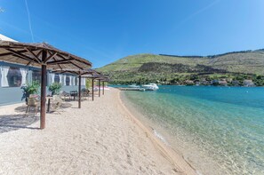 Ein Strand mit klarem Wasser, einer Holzkonstruktion mit Stühlen und Booten im Hintergrund.