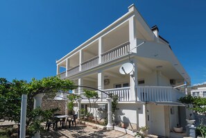 En toetages bygning med balkon, udendørs siddepladser og krukker med planter.