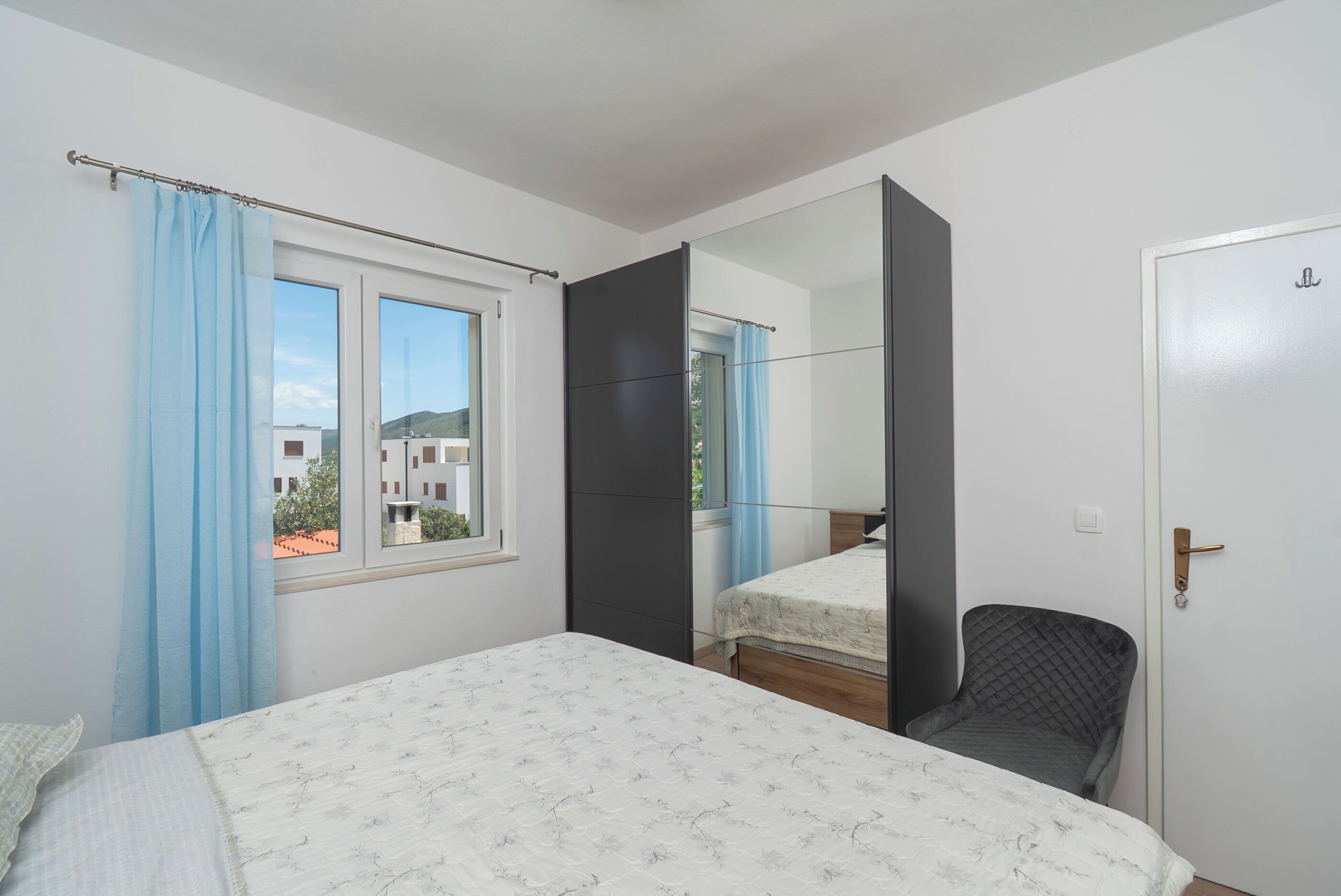 Un dormitorio con cama, una silla, una ventana con cortinas y una puerta.