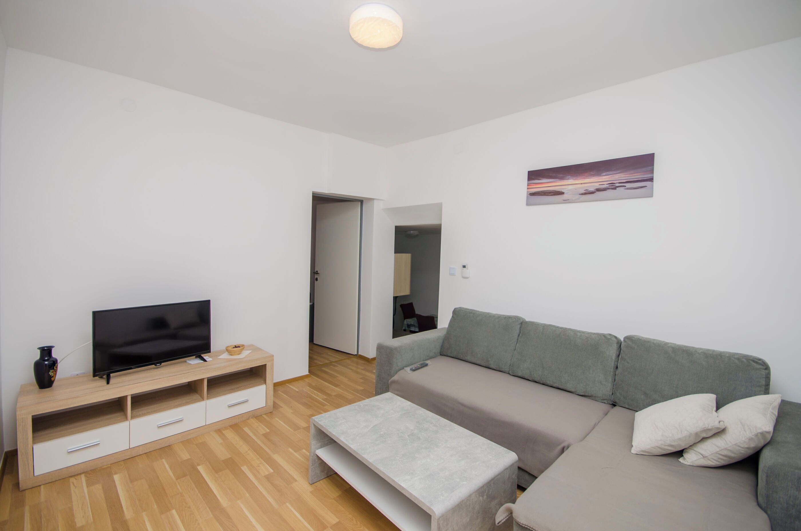A modern living room with a flat-screen TV on a wooden TV stand, a grey sofa, and a small coffee table.