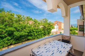 A balcony with a table and chairs, overlooking a garden and buildings. - Apartments Mirjana (Nin)