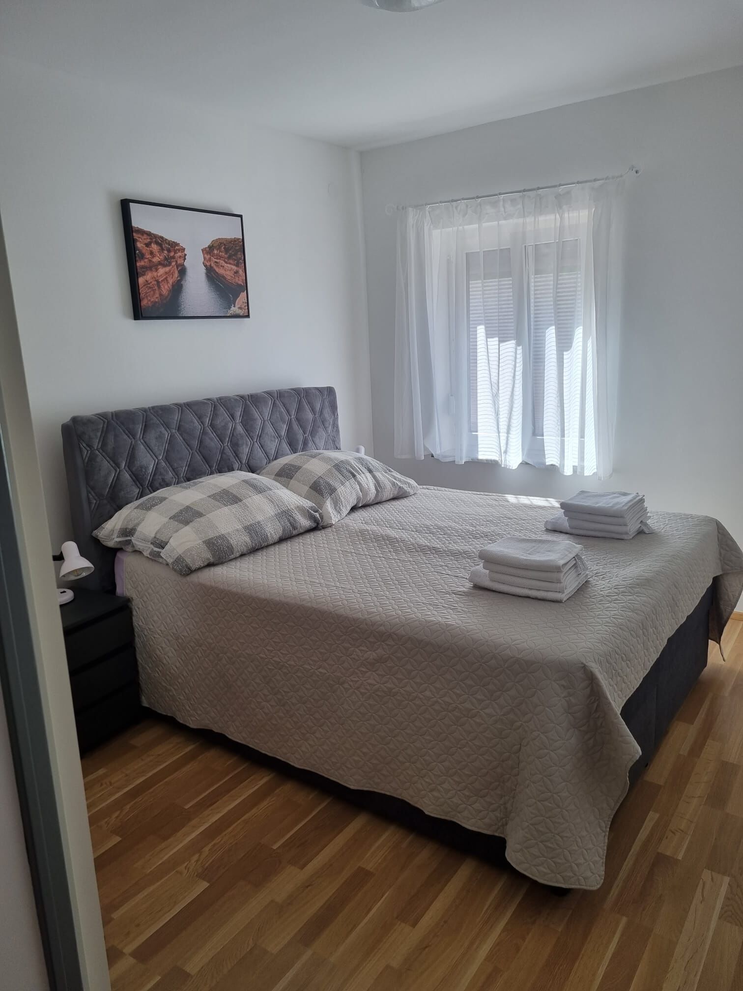 Un lit bien fait, avec une couverture matelassée, un oreiller et des serviettes pliées, posé sur un plancher en bois.