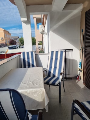 A balcony with a table and striped chairs, a view of buildings, and a parked car. - Apartments Mirjana (Nin)