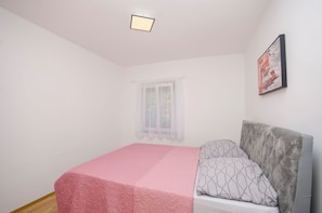 A bedroom with a bed, a window with sheer curtains, a framed picture on the wall, and a ceiling light. - Apartments Mirjana (Nin)