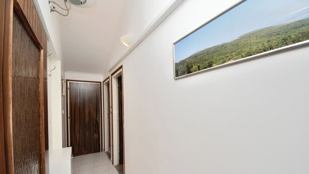 Un couloir avec une porte en bois, un mur blanc orné d’un tableau encadré et un sol carrelé.