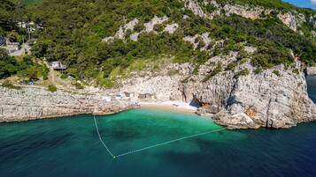 A coastal area with a rocky beach, clear turquoise waters, and a small building near the shore.