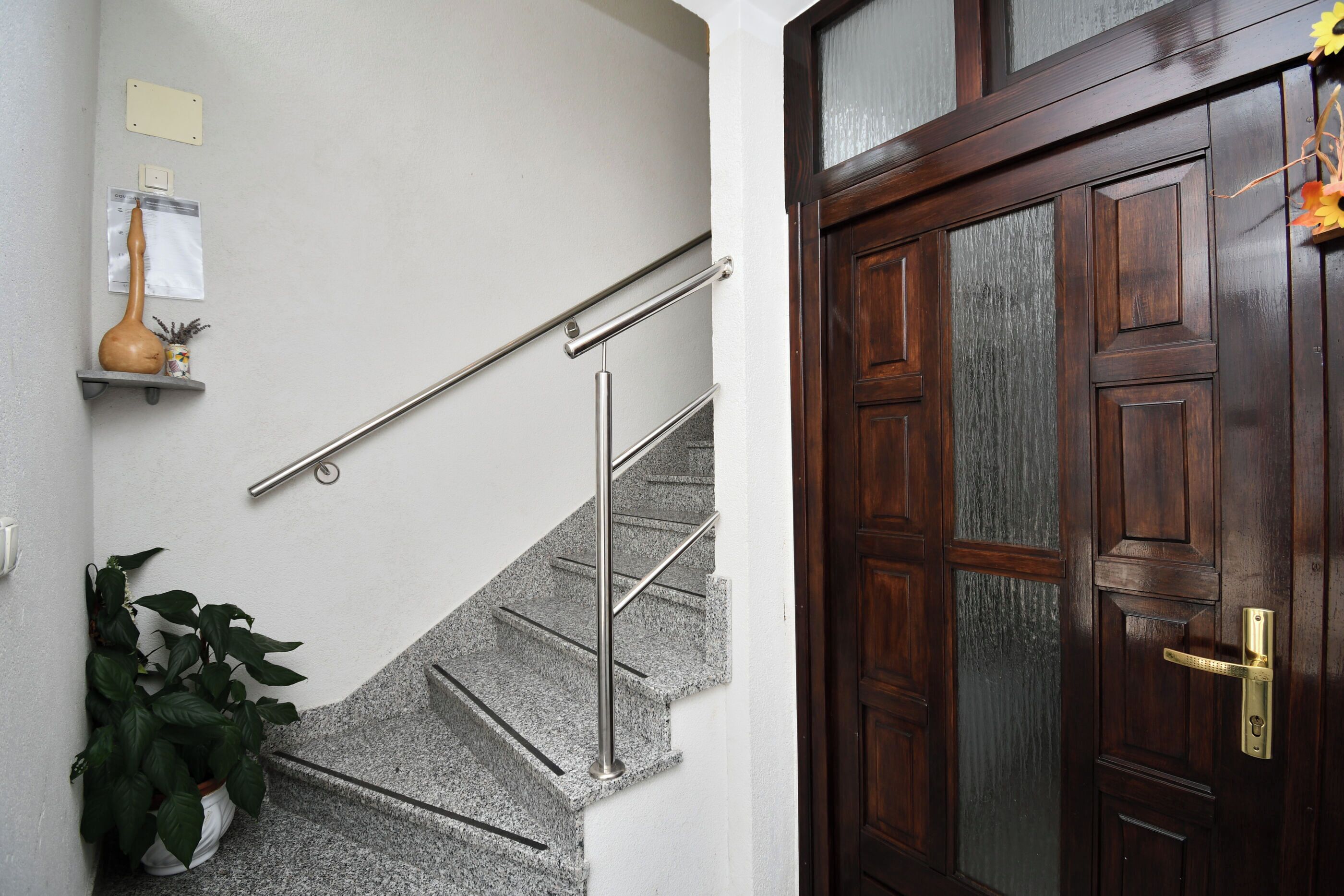 Una escalera con barandillas de metal, una puerta de madera con pomo de latón y una planta en maceta a la izquierda.