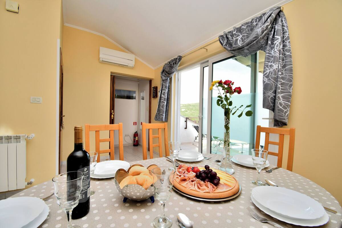 A dining table set with plates, glasses, a bottle, bread, and a fruit platter.