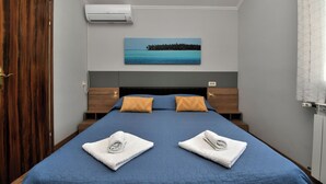 Camera d'albergo con un letto, un armadio in legno, condizionatore d'aria e un quadro raffigurante una spiaggia.