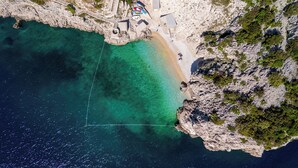Une vue aérienne d’une zone côtière avec une plage de sable fin, des falaises rocheuses et un petit bâtiment doté d’un quai.
