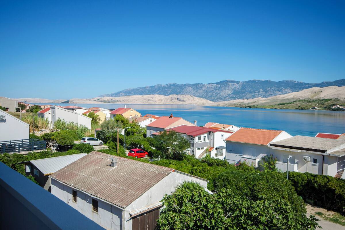 A coastal residential area with houses, a red car, and a lake with mountains in the background.