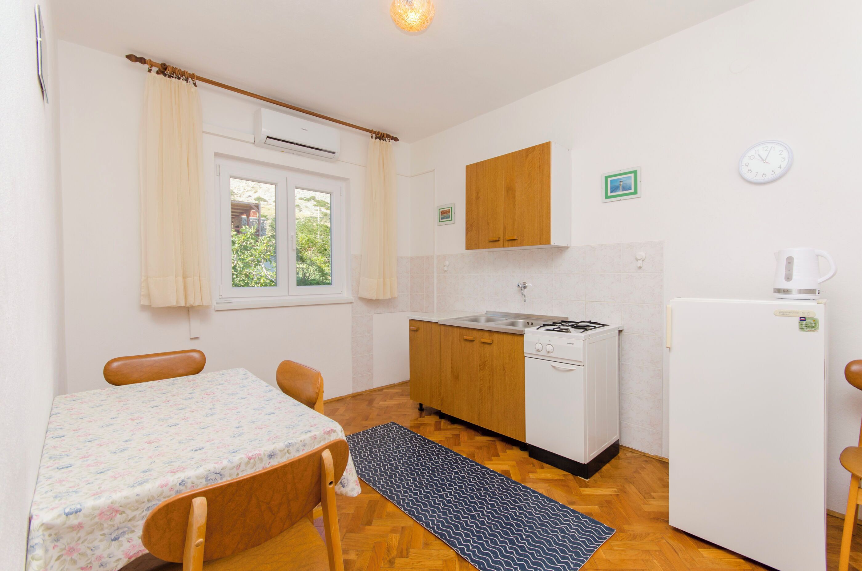 Una cocina compacta con una mesa de comedor, sillas, estufa, refrigerador y una ventana con cortinas.