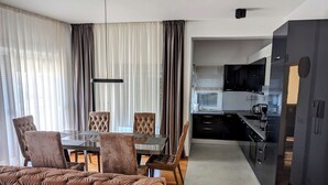 A modern living room with a glass dining table, tufted sofas, and a view into the kitchen. - Apartment Penthouse (Split)