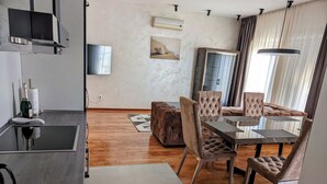 A modern living room with a dining area, wooden flooring, a flat-screen TV, and a large window with curtains. - Apartment Penthouse (Split)