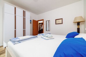 A hotel room with a bed, a wardrobe, a mirror, a lamp, and a door leading to a bathroom. - Apartment Anita (Crikvenica)