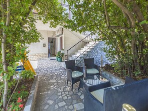 A stone-paved outdoor area with wicker furniture, a staircase, and a view of the building's interior. - Apartment Anita (Crikvenica)