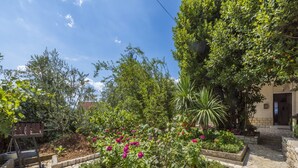 Une cour bordée de sentiers en pierre, entourée d’une végétation luxuriante et de plantes en fleurs.