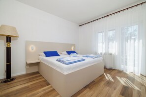 A modern bedroom with a large bed, bedside lamps, and a view of the outdoors through sheer curtains. - Apartment Anita (Crikvenica)