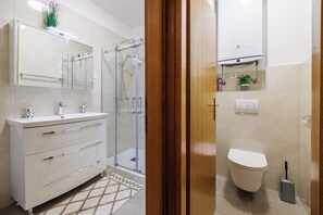 A bathroom with a glass shower enclosure, a white toilet, and a sink with a mirror above it. - Apartment Anita (Crikvenica)