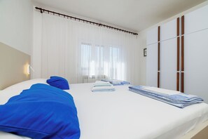 A hotel room with a bed, a window with curtains, a wardrobe, and a bedside table. - Apartment Anita (Crikvenica)