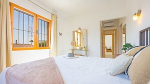 Ein Schlafzimmer mit einem großen Bett, einem Nachttisch, einem Spiegel und einem Fenster mit Vorhängen.