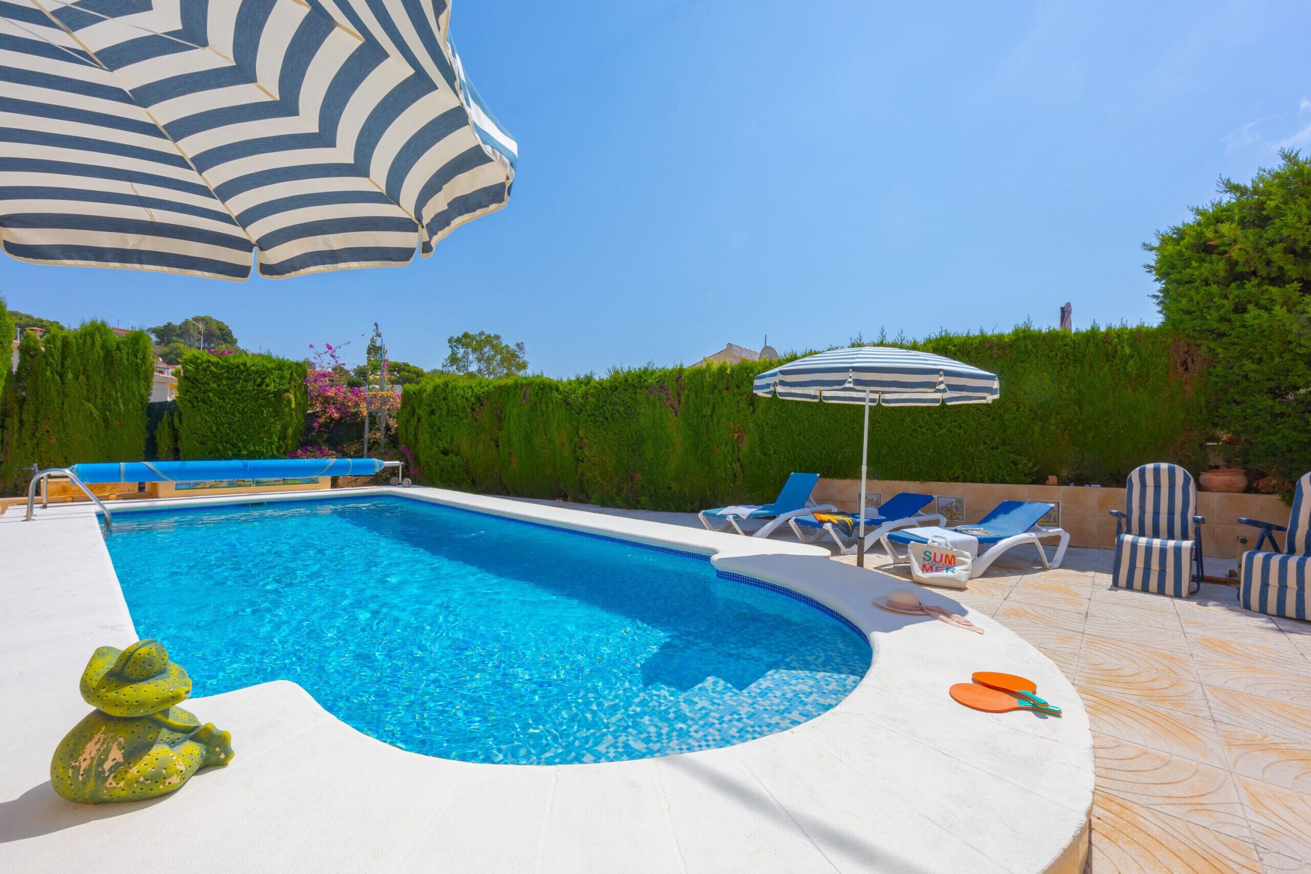 A swimming pool with lounge chairs and umbrellas, surrounded by greenery.