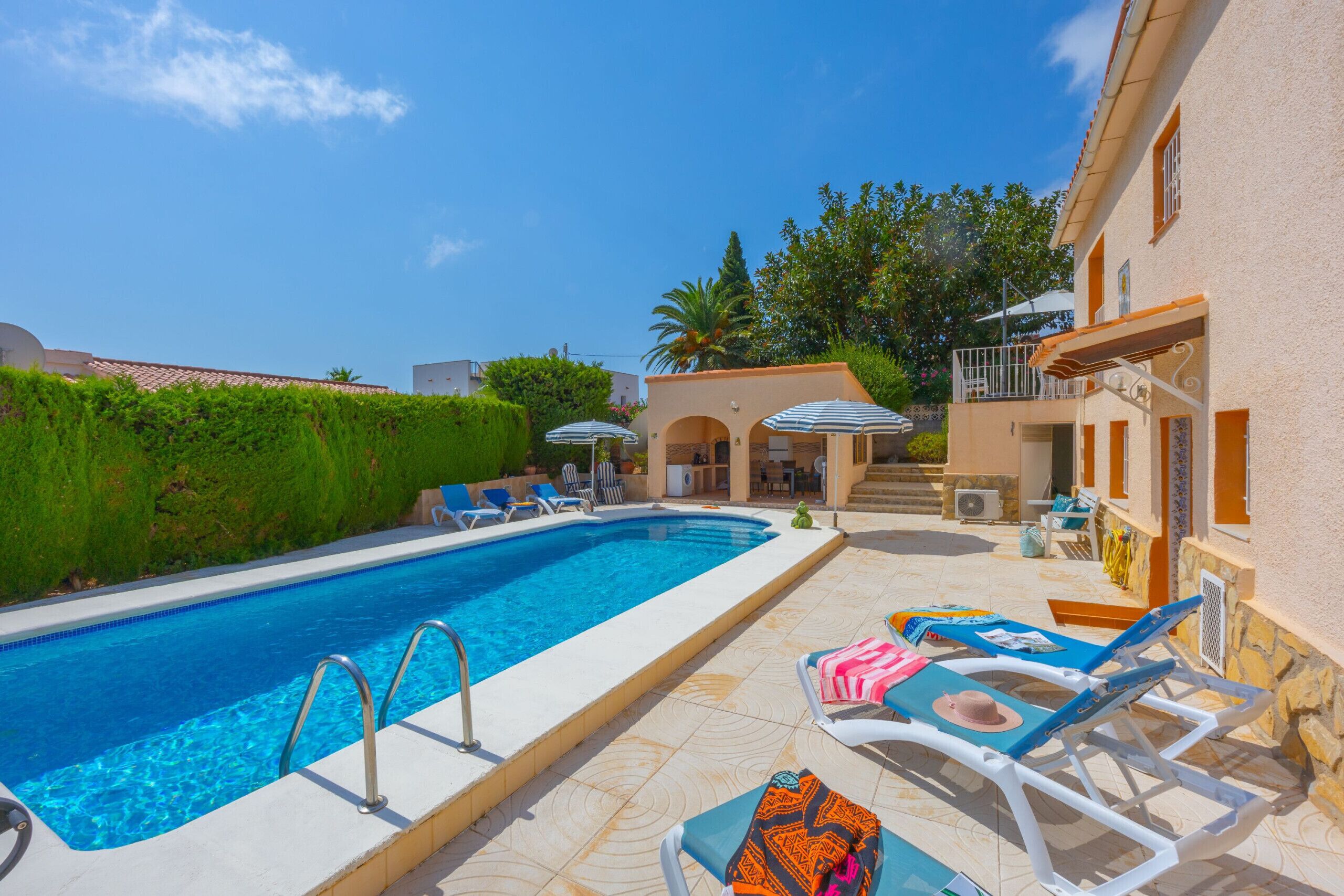 A swimming pool with lounge chairs and umbrellas, surrounded by a building with a tiled patio.