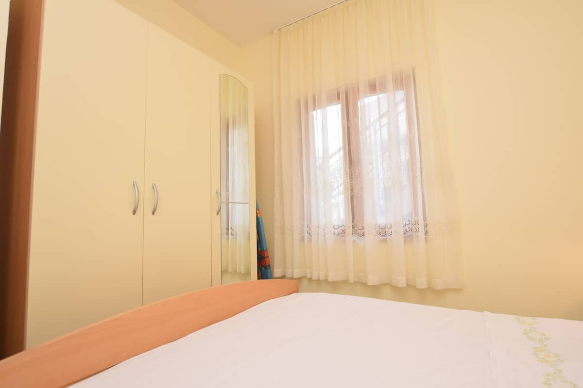 A bedroom with a bed, a wardrobe, and a window with sheer curtains.