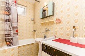 Een badkamer met behang met een patroon, een wit wastafelmeubel, een spiegel, een handdoekhouder en een douchegordijn met een stadsgezicht.