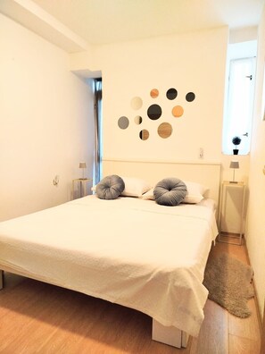 A bedroom with a large bed, a wall art piece, and a window with a view. - Apartments Rose (Sibenik)