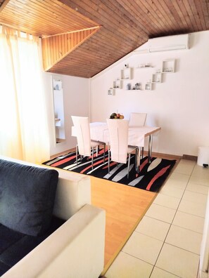 A modern living room with a sofa, a dining area with a table and chairs, and a kitchen area with a refrigerator and shelves. - Apartments Rose (Sibenik)