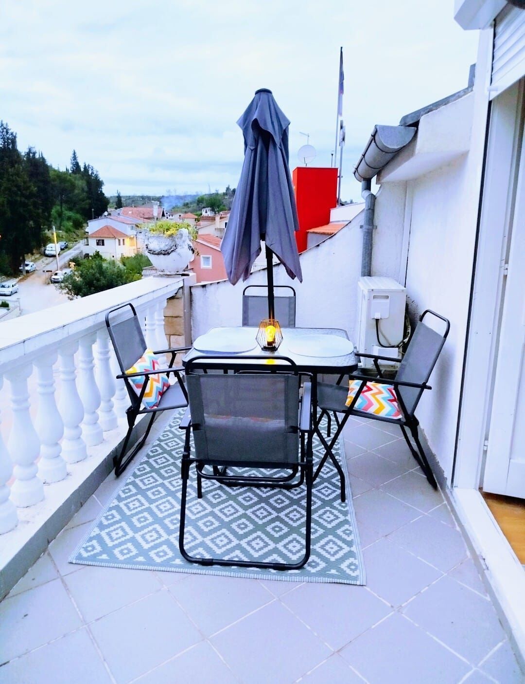 A balcony with a table and chairs, a patterned rug, and a grey umbrella.