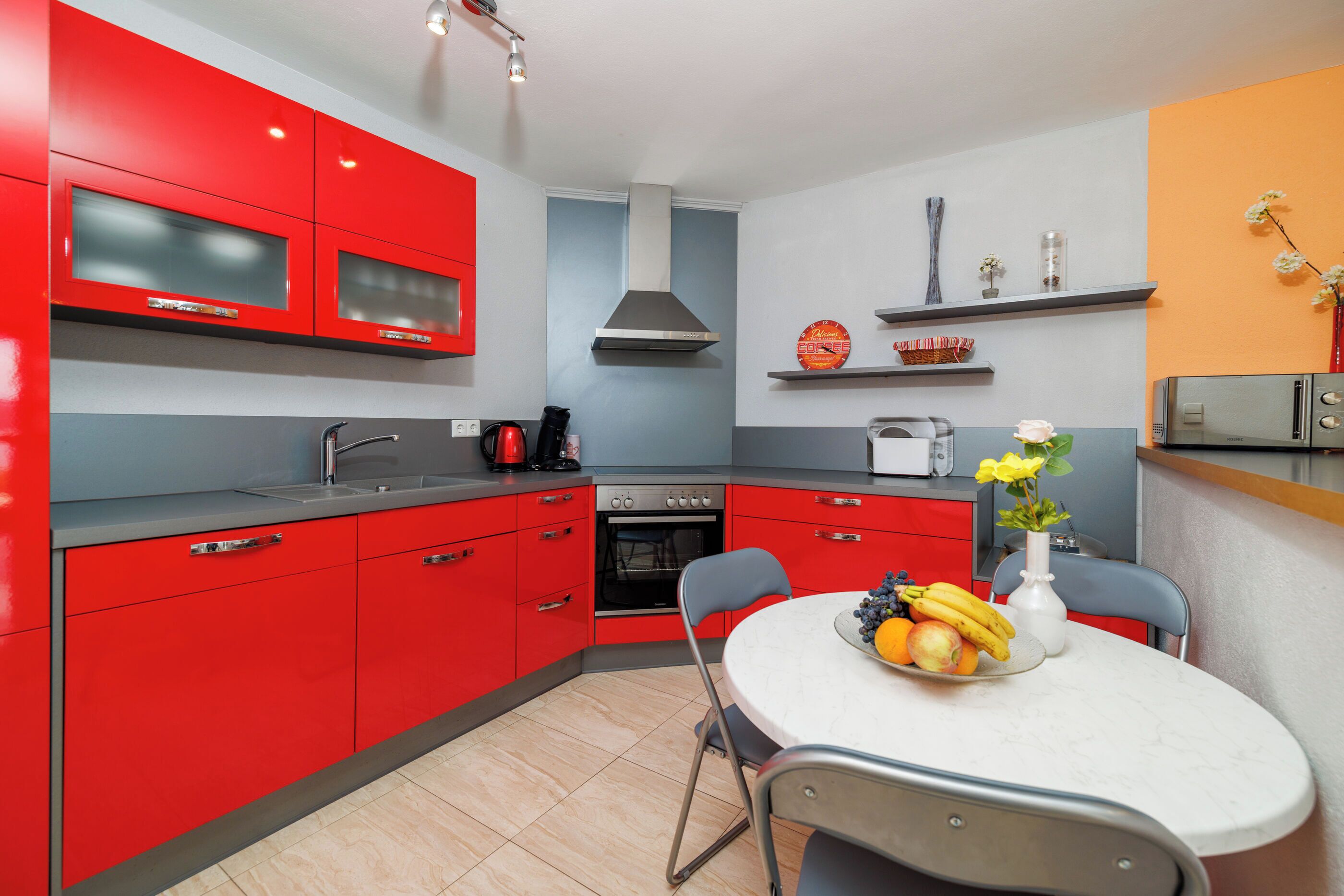 Una cocina moderna con armarios rojos, encimera blanca y un comedor con una mesa dispuesta para dos personas.