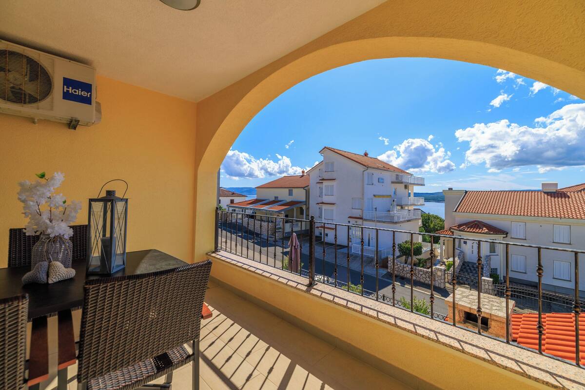 Ein Balkon mit Korbmöbeln, einer Laterne und Blick auf Gebäude sowie ein Gewässer.