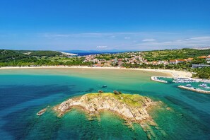 A coastal town with a beach, clear waters, and a rocky outcrop. - Apartments Rasic (Rab)
