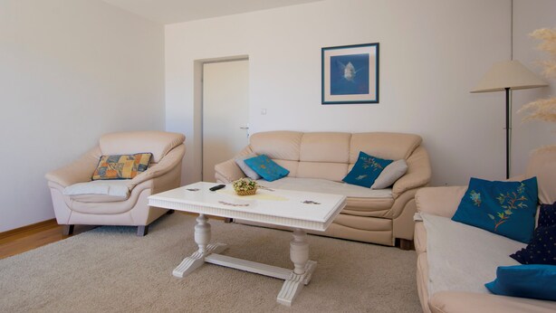 A living room with a beige sofa, a white coffee table, and a beige armchair.