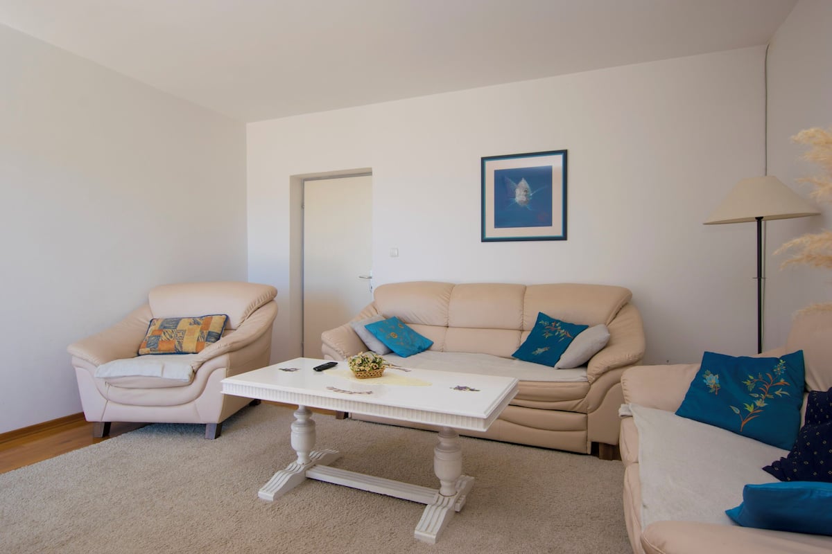 Una sala de estar con un sofá color beige, una mesa de centro blanca y un sillón color beige.