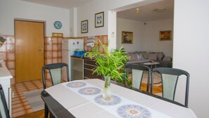 A dining area with a table set for four, a vase with green plants, and a kitchen in the background.
