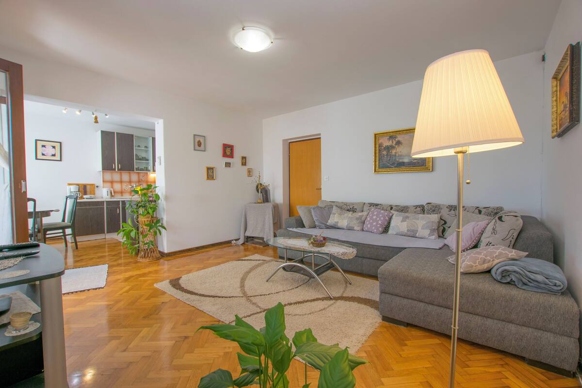 Una sala de estar con sofá, mesa de centro y lámpara. Hay un comedor con mesa y sillas. El piso es de madera y tiene una alfombra.