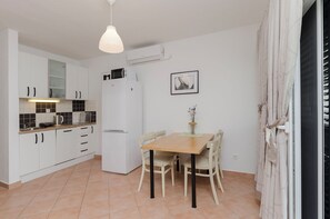 A compact kitchen with white cabinets, a microwave, a refrigerator, and a dining table with chairs. - Apartment Rose Garden (Rovinj)