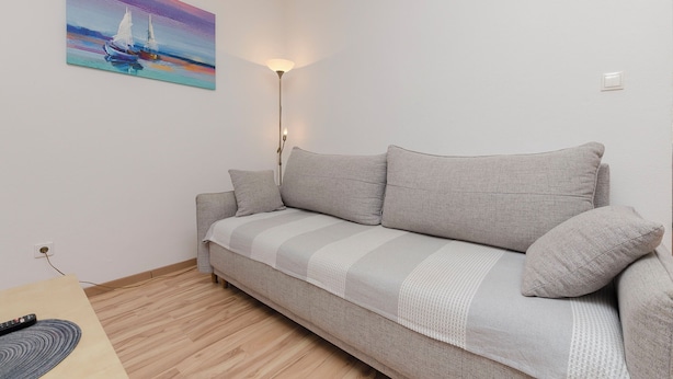 A living room with a sofa, a painting, a floor lamp, and a remote control on a table. - Apartment Rose Garden (Rovinj)